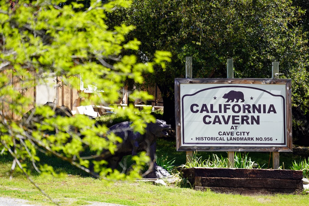 Schild der California Cavern in Cave City, Kalifornien, mit grünem Blattwerk im Vordergrund