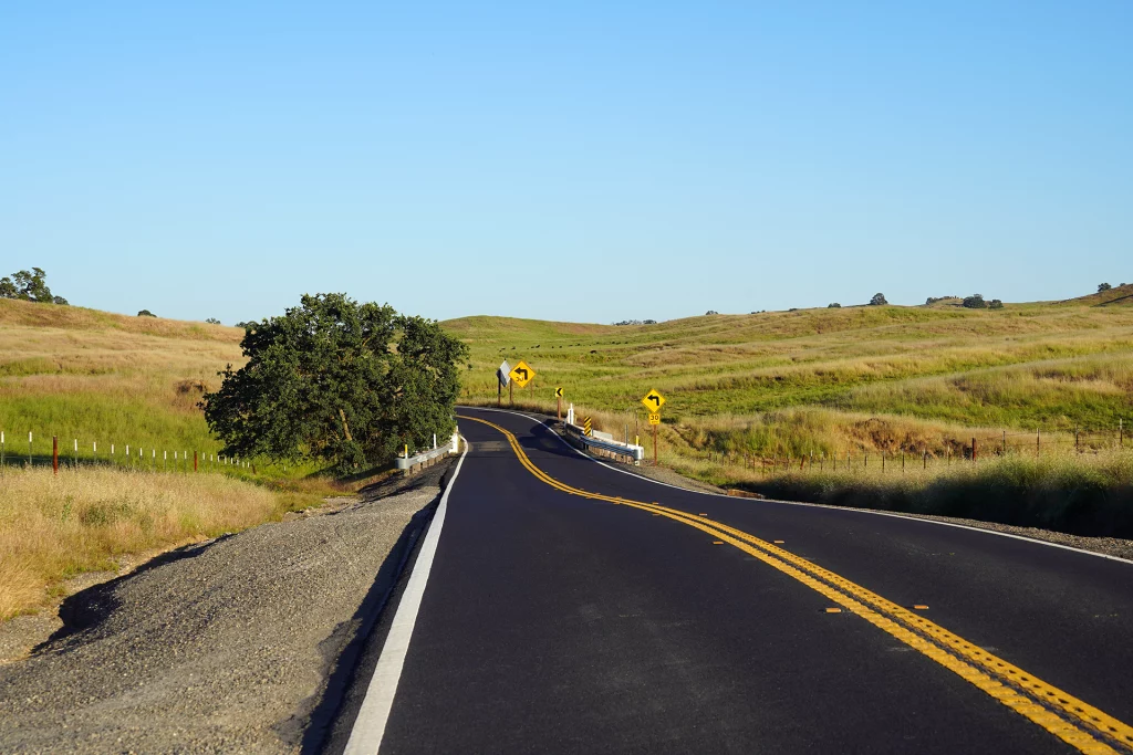 Kurviger Highway 132 durch hügelige Graslandschaft bei La Grange, Kalifornien