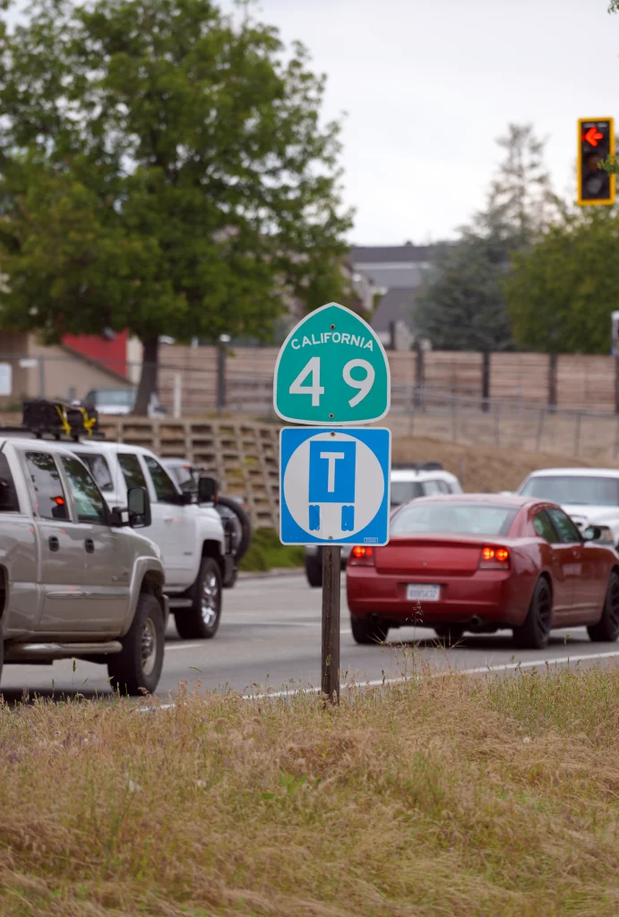Straßenschild der California State Route 49 mit Verkehrszeichen für LKW-Wendepunkt, im Hintergrund Autos im Stadtverkehr