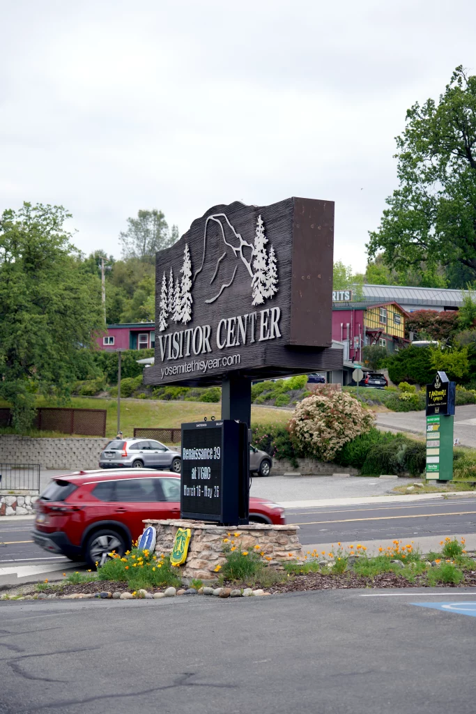Hinweisschild des Visitor Centers in Oakhurst bei Yosemite National Park mit vorbeifahrenden Autos im Vordergrund