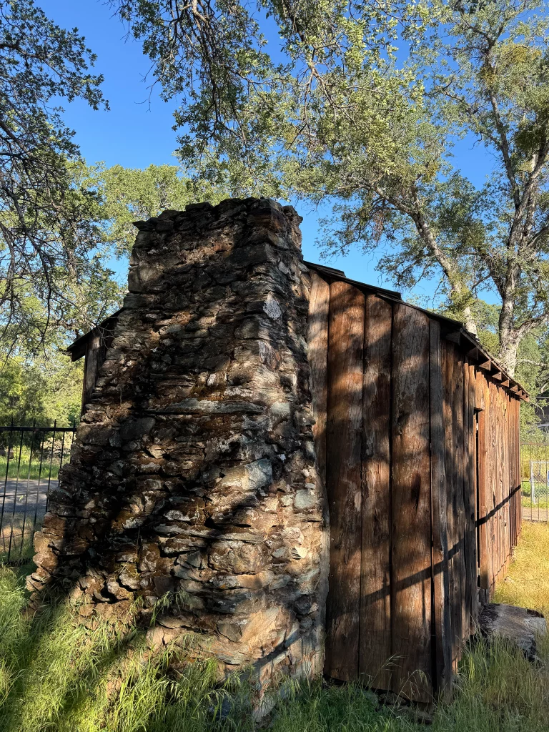 Rückseite der Mark Twain Cabin mit gemauertem Steinkamin unter Eichenbäumen, Kalifornien