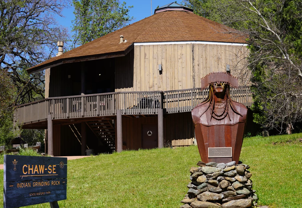 Holzgebäude und Skulptur im Chaw’se Indian Grinding Rock State Historic Park, Kalifornien