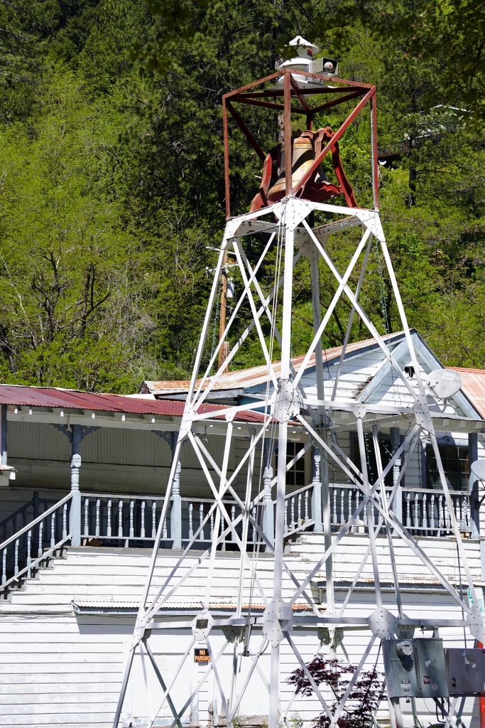 Historischer Glockenturm mit Metallgestell vor einem alten Holzgebäude in Downieville, Kalifornien