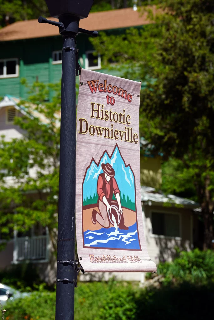 Willkommensschild „Welcome to Historic Downieville – Established 1849“ mit Goldwäscher-Illustration an einer Laterne im Ortszentrum