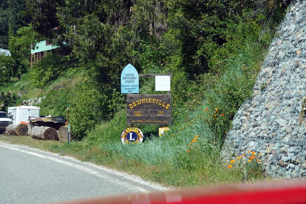 Ortsschild von Downieville, Kalifornien, an der Straße mit Blumen, Wald und einem Hinweis auf die United Methodist Church