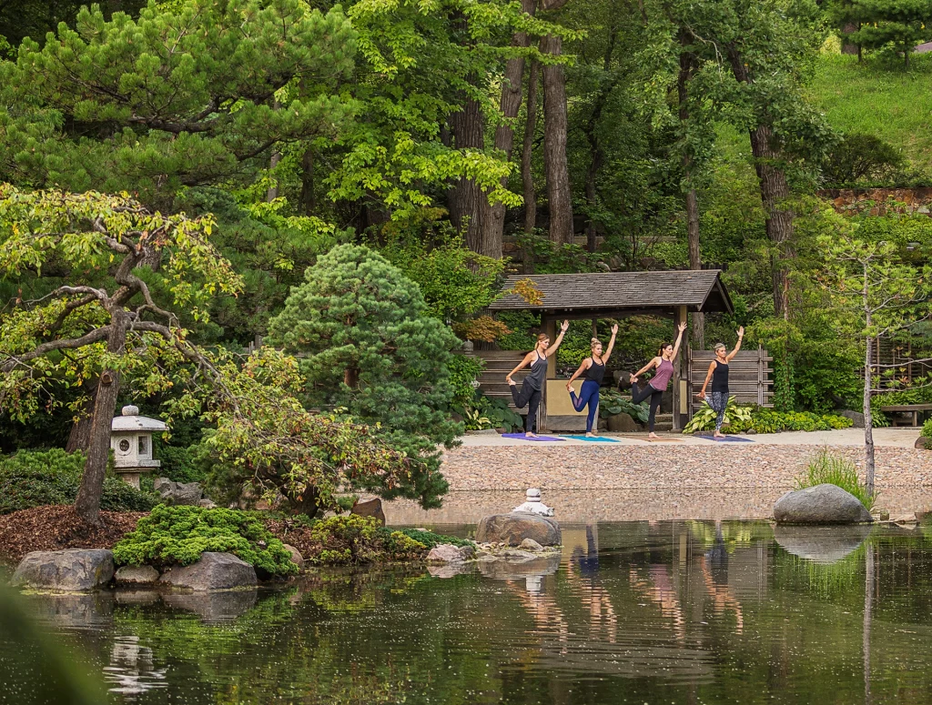 Yoga-Gruppe beim Training im Anderson Japanese Garden vor üppigem Grün und Teich.