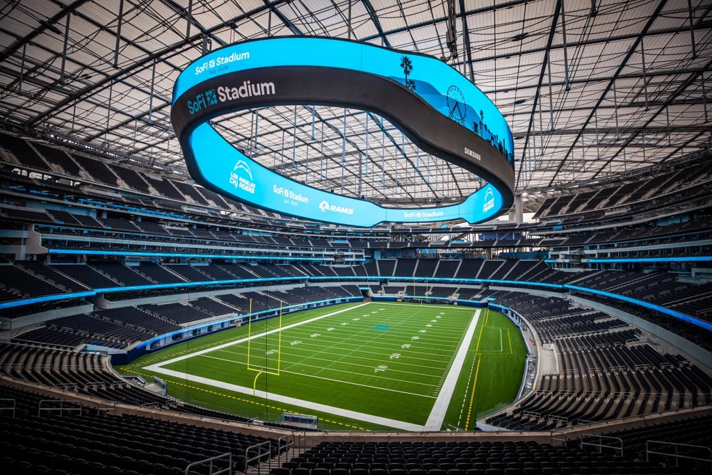 Wide-angle interior view of the SoFi Stadium in Inglewood, California, showcasing its modern architecture and massive video board above the football field.