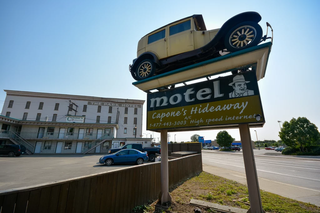 Motel-Schild von Capone’s Hideaway mit Oldtimer und The Park Hotel im Hintergrund in Moose Jaw, Saskatchewan