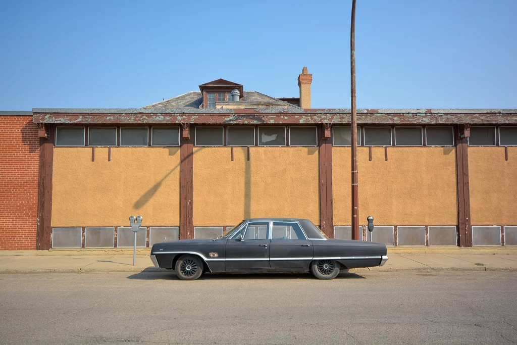 Oldtimer parkt vor verwitterter gelb-brauner Fassade in der Innenstadt von Moose Jaw, Saskatchewan
