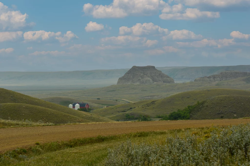 Castle Butte in der weiten Prärie von Saskatchewan mit einer roten Scheune und Getreidesilos im Vordergrund.
