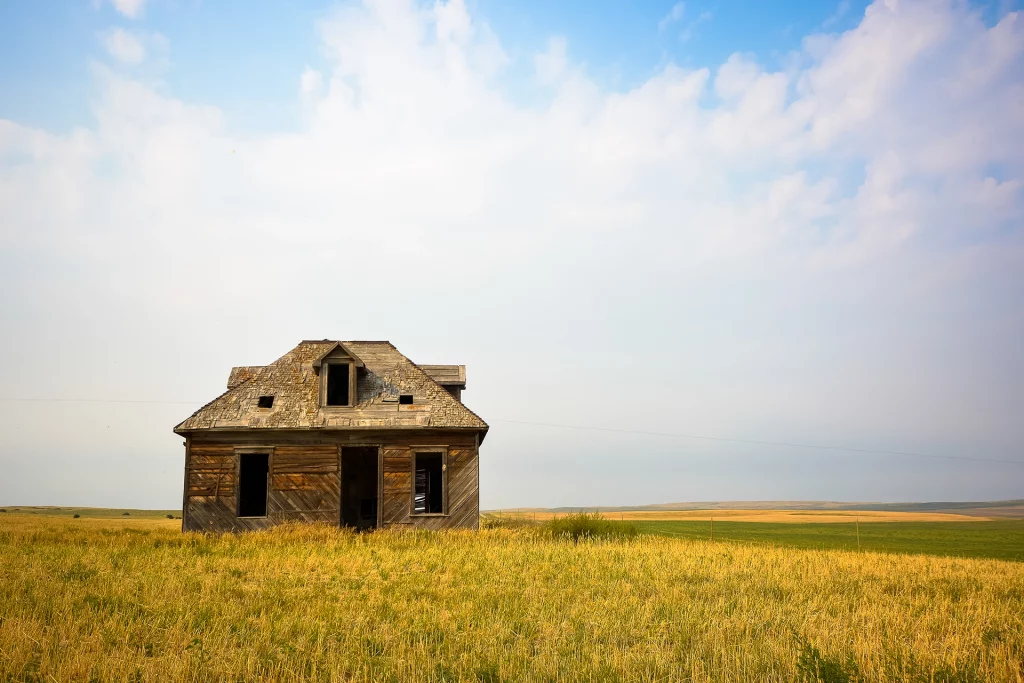 Verfallenes Farmhaus aus Holz inmitten goldener Präriegraslandschaft in Saskatchewan unter blauem Himmel