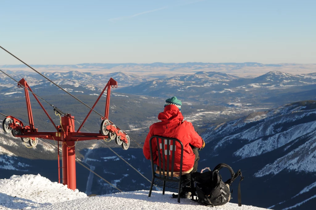 Skipatrouilleur im roten Outfit mit Blick über die verschneite Landschaft im Castle Mountain Resort, Alberta.
