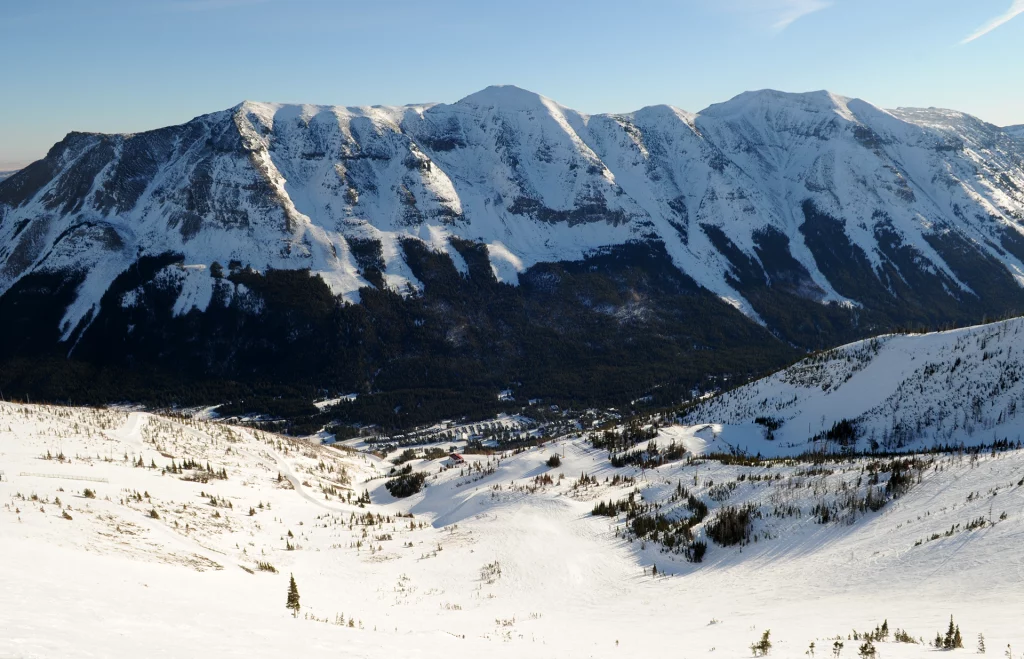 Blick auf die schneebedeckten Hänge des Castle Mountain Resorts in Alberta mit markanter Gebirgskette im Hintergrund.