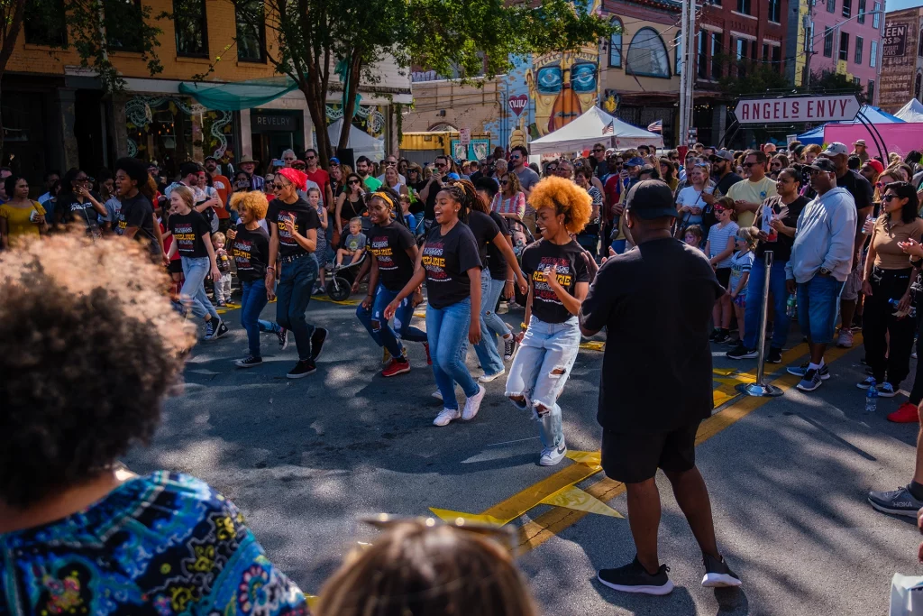 Tanzgruppe performt bei Sonnenschein auf dem NULU Fest in Louisville vor einer begeisterten Menschenmenge.