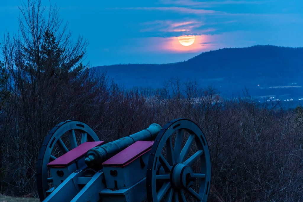 Kanone im Saratoga National Historical Park bei Sonnenuntergang mit Vollmond über den Bergen.