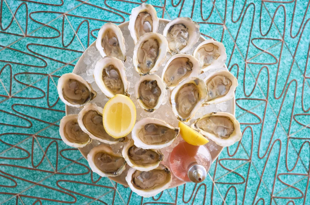Platte mit frischen Austern auf Eis, serviert mit Zitrone und Mignonette-Soße.