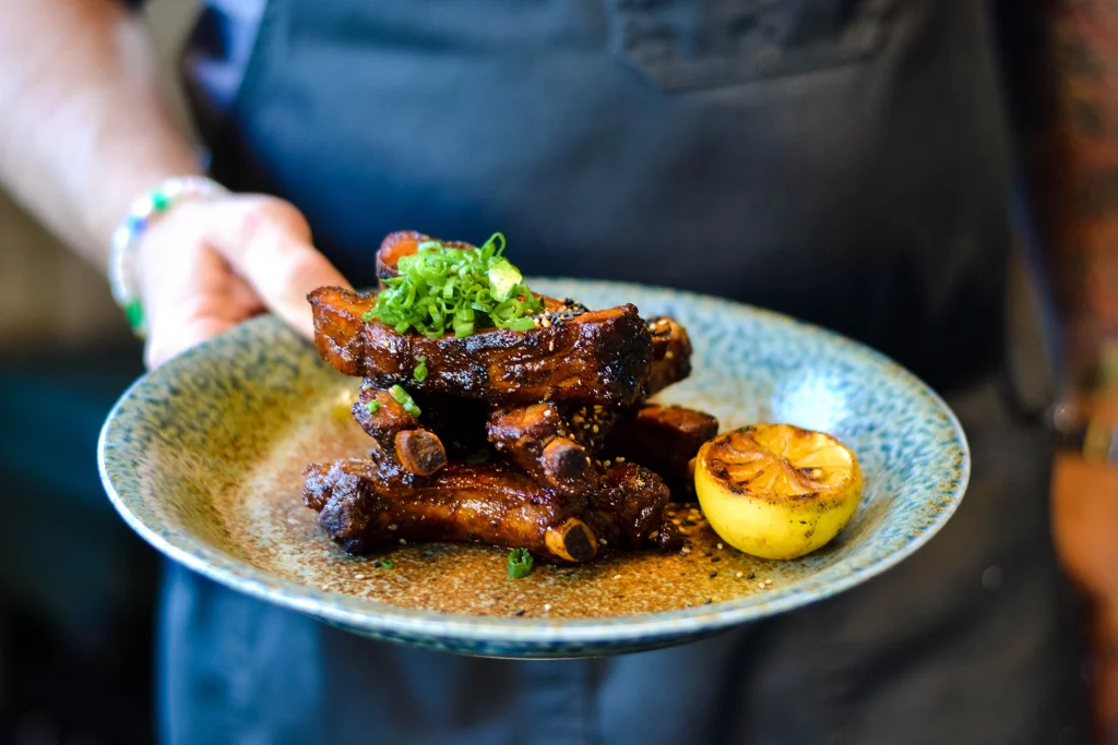 Teller mit glasierten Baby Back Ribs, garniert mit Frühlingszwiebeln, serviert mit gegrillter Zitrone im Ukiah Japanese Smokehouse.