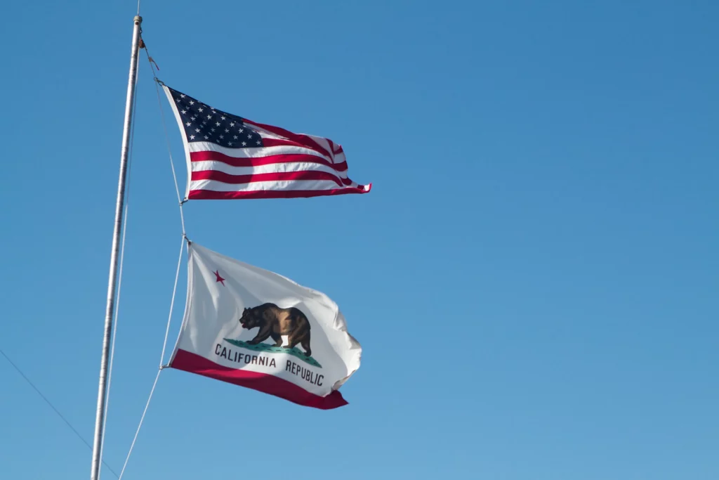 US-Flagge und Kalifornien-Flagge wehen nebeneinander vor blauem Himmel.