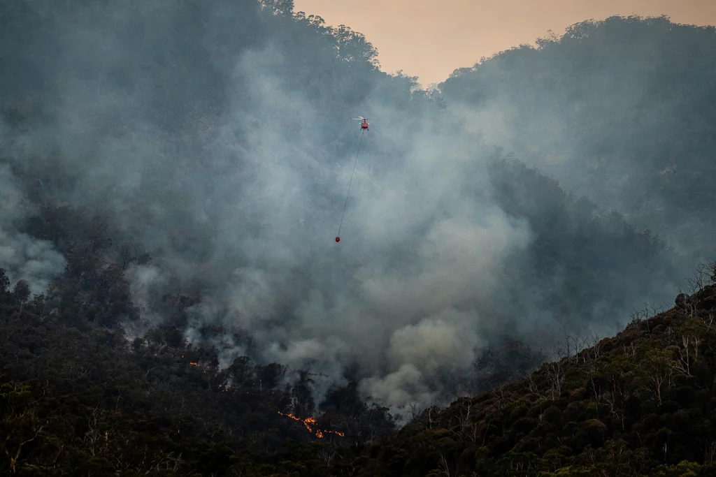 Löschhubschrauber fliegt über rauchverhüllte Berge, um Waldbrand zu bekämpfen.