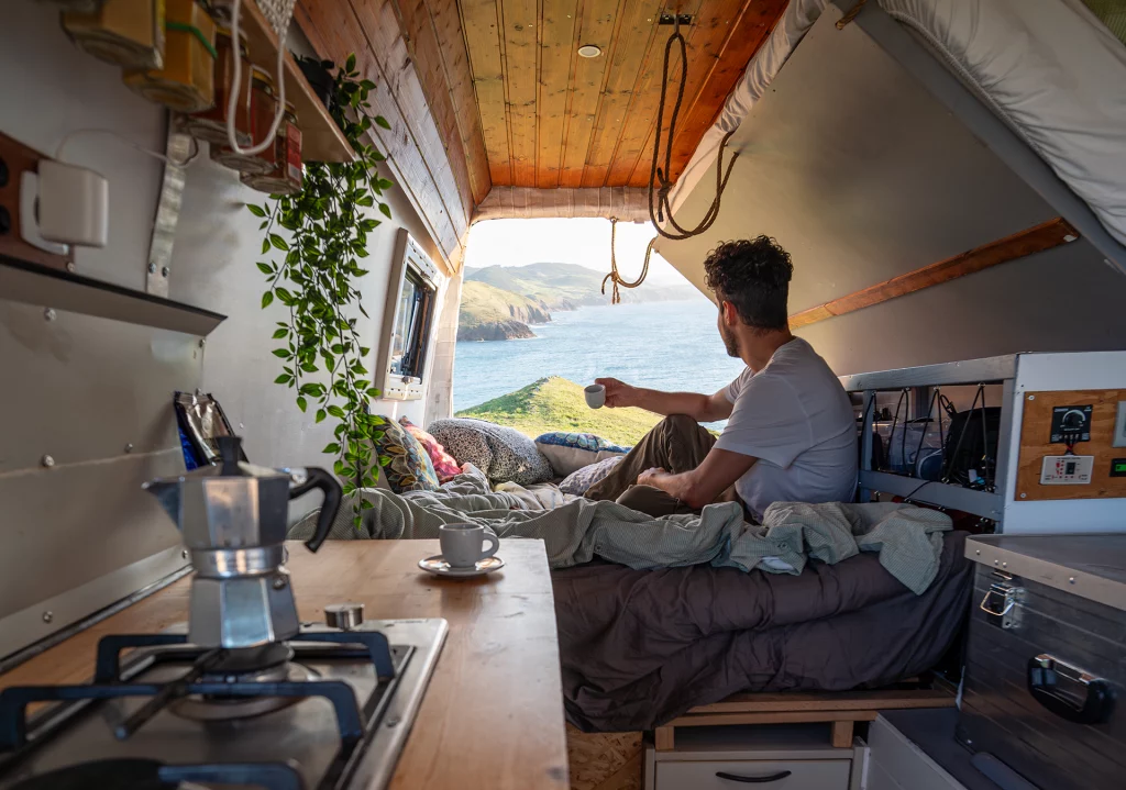 Mann genießt Kaffee im Bett seines Campervans mit Blick aufs Meer