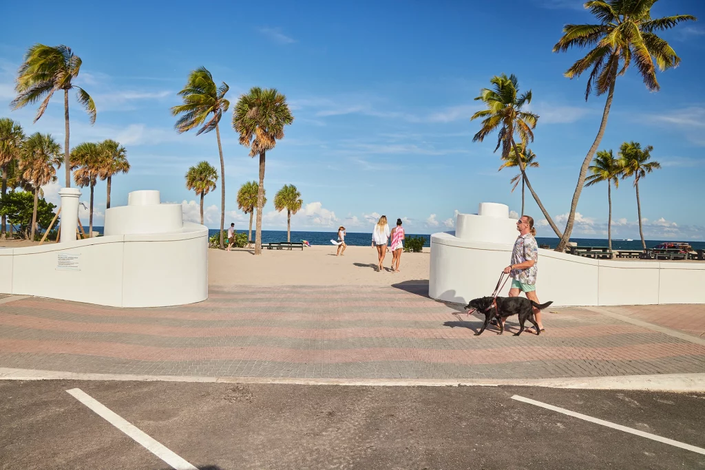 Eingang zum Strand von Fort Lauderdale mit weißen Torbögen, Palmen und Spaziergängern.
