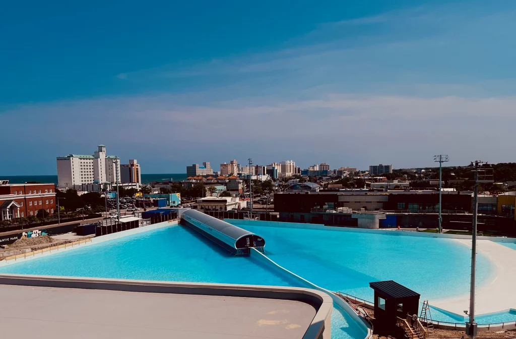 Blick von oben auf den Atlantic Park Surf Wavepool in Virginia Beach mit Skyline und Atlantikküste im Hintergrund.