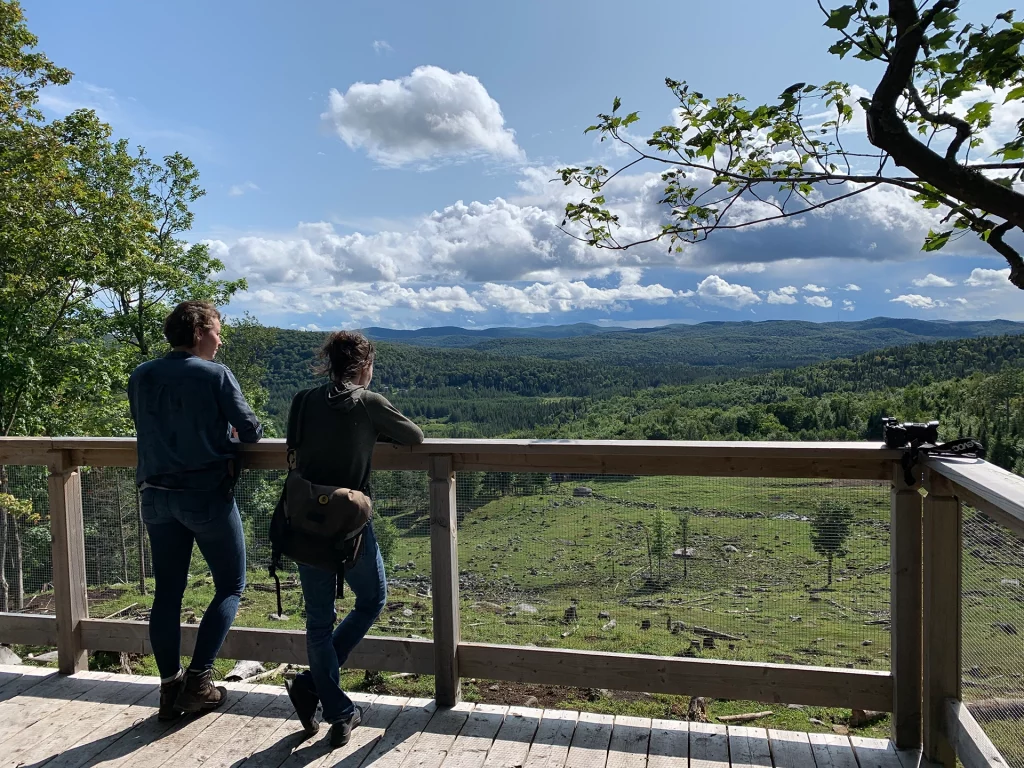 Zwei Besucher genießen von einer Holzplattform im Park Kanatha-Aki den weiten Blick über Wälder und Berge in den Laurentiden.