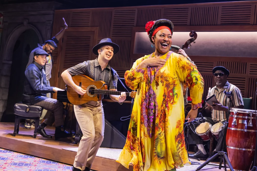 Szene aus dem Broadway-Musical Buena Vista Social Club mit Sängerin in gelbem Kleid, Gitarrist und Band im Hintergrund.