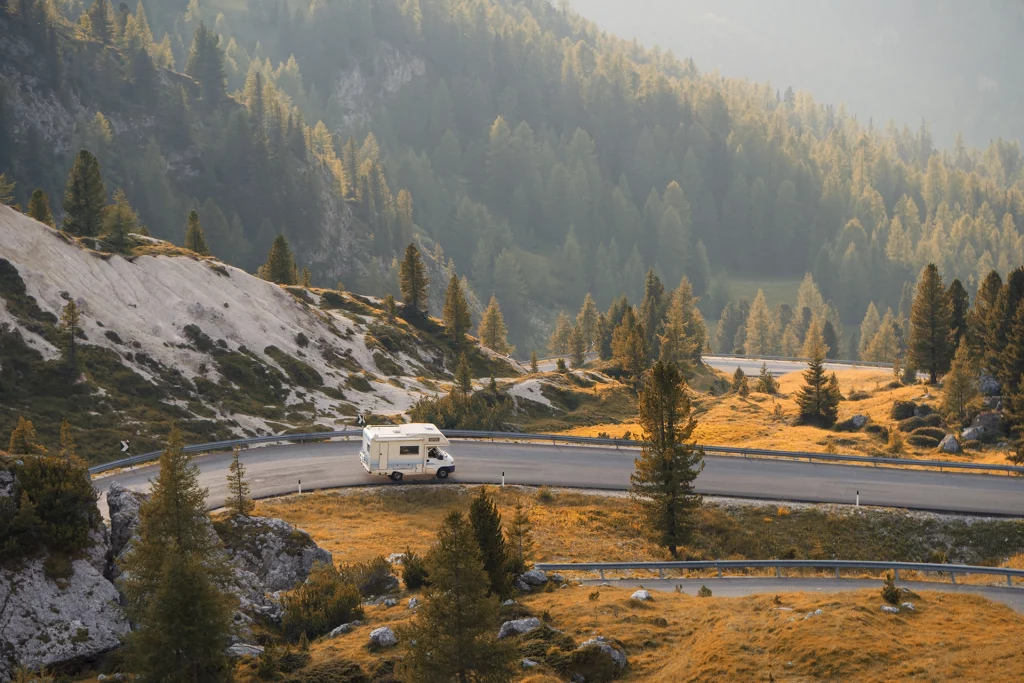 Wohnmobil auf Serpentinenstraße in den Alpen, umgeben von Berglandschaft bei goldenem Abendlicht