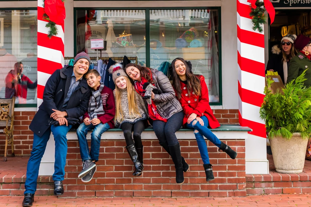 Fröhliche Familie posiert beim Weihnachtseinkauf in Port Jefferson vor festlich dekorierten Schaufenstern.