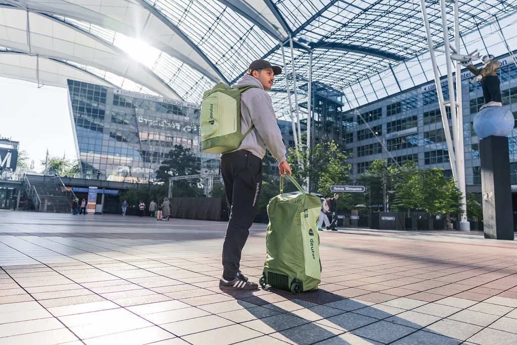 Mann mit grünem Deuter Duffel Pro Roller Trolley und passendem Rucksack im Innenhof des Münchner Flughafens.