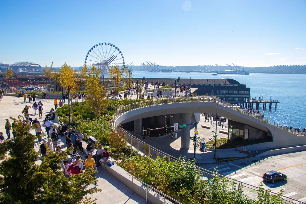 Spaziergänger auf dem Overlook Walk im neuen Waterfront Park in Seattle mit Riesenrad und Blick auf den Puget Sound.