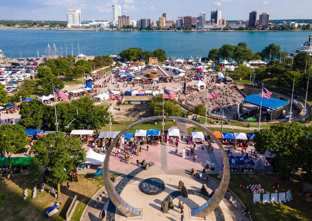 Luftaufnahme des African World Festival am Detroit River mit bunten Marktständen und Blick nach Windsor, Kanada.