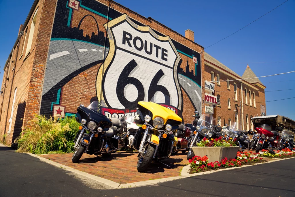 Motorräder parken vor einer großen Route 66 Wandmalerei an einem Backsteingebäude.