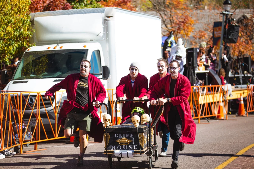 Teilnehmer beim Emma Crawford Coffin Race in Manitou Springs schieben einen sargähnlichen Wagen die Straße hinunter.