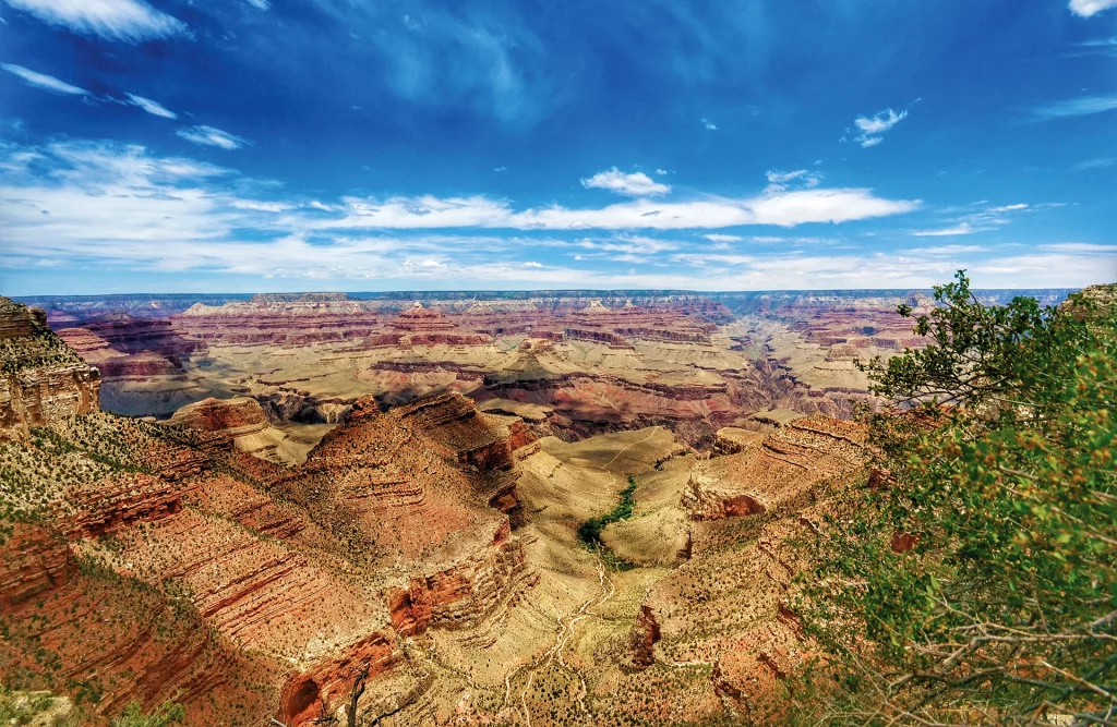 Weitwinkelaufnahme des Grand Canyon South Rim mit dramatischer Felslandschaft und blauem Himmel.