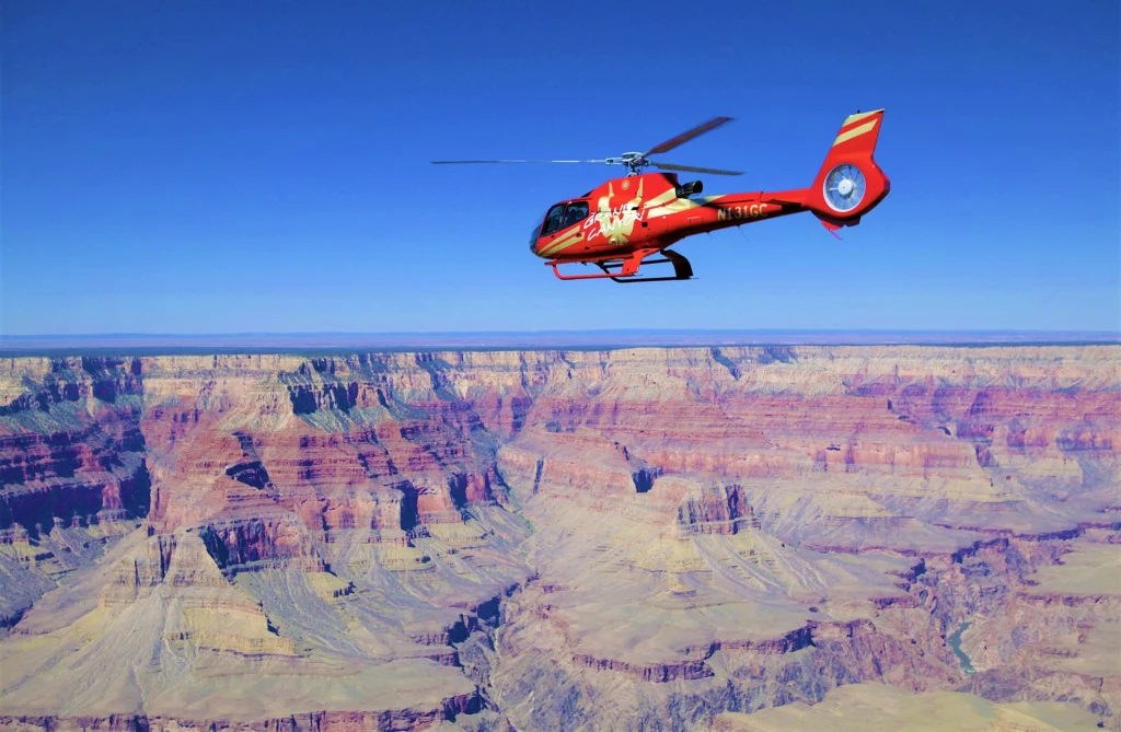 Roter Papillon-Helikopter fliegt über die tiefen Schluchten des Grand Canyon bei klarem Himmel.