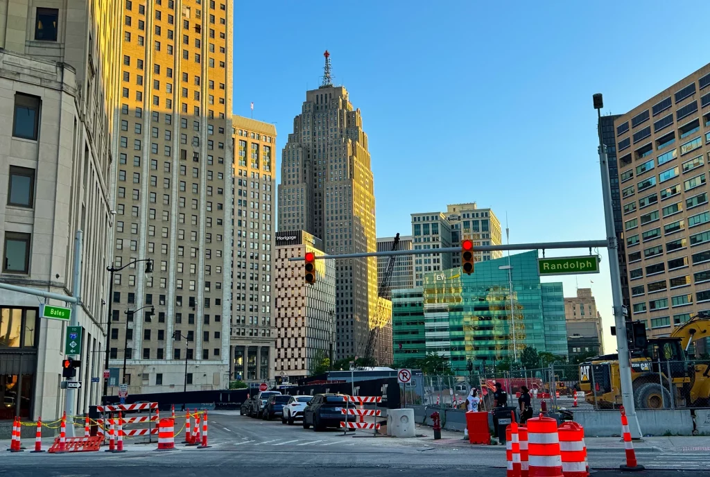 Straßenszene mit Baustellen, Absperrungen und Hochhäusern in Downtown Detroit bei Abendlicht.