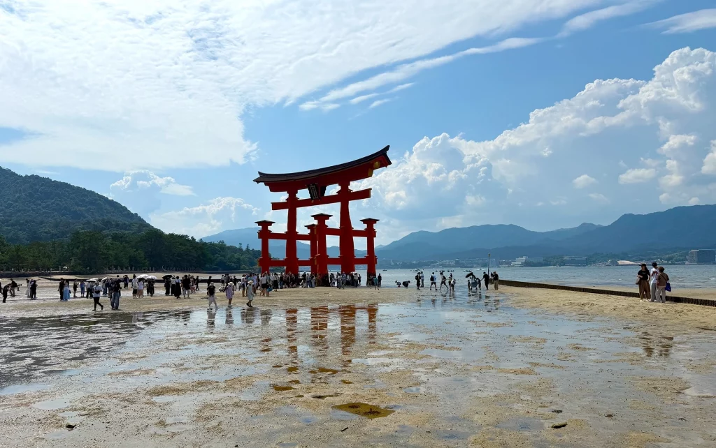 Großes rotes Torii im Wasser vor Miyajima bei Ebbe mit vielen Besuchern.