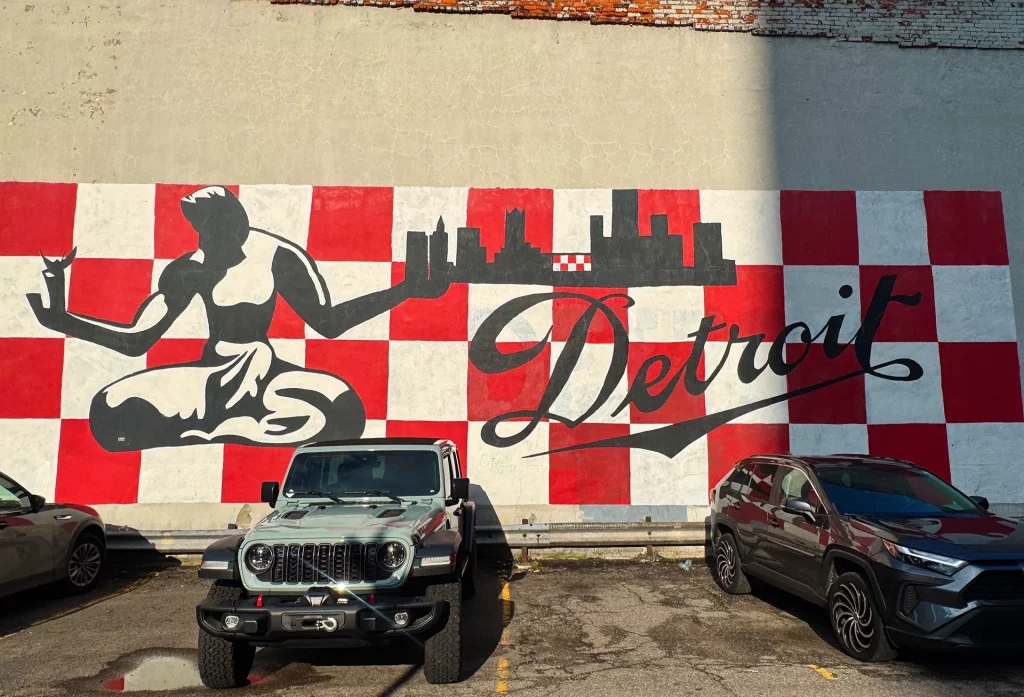 Großes Wandgemälde des Spirit of Detroit in Rot-Weiß mit Skyline-Silhouette und Schriftzug „Detroit“.
