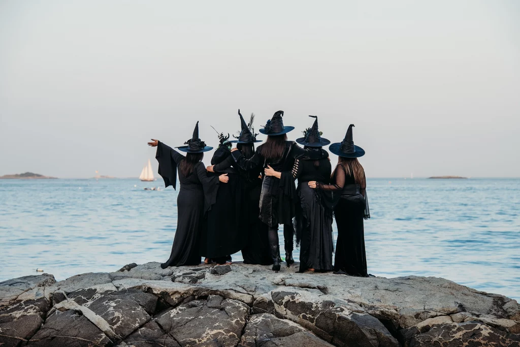Gruppe verkleideter Frauen in Hexenkostümen posiert auf Felsen am Meer in Salem, Massachusetts.