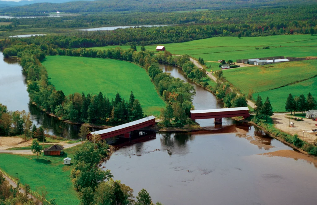 Historische rote Zwillingsbrücken Ferme-Rouge in Kiamika über einem Fluss, eingebettet in grüne Landschaft.