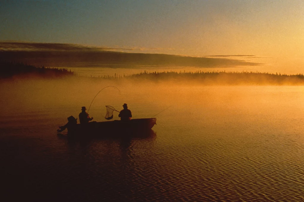 Zwei Angler im Boot werfen ihre Ruten im Sonnenuntergang auf einem stillen See im Parc national du Mont-Tremblant.