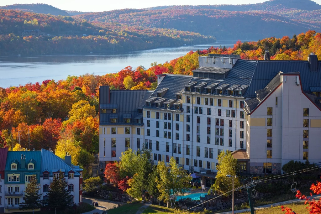 Das Fairmont Tremblant Hotel im Herbst, umgeben von buntem Laub und Blick auf den See, Laurentides, Québec.