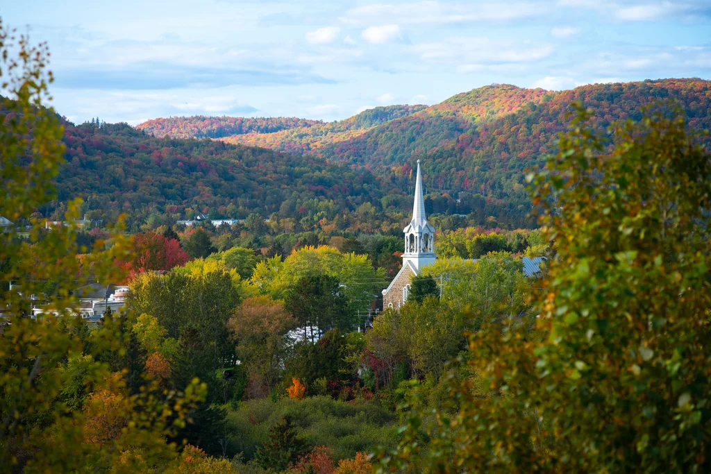 Kirche von Saint-Jovite zwischen herbstlichen Bäumen vor Berglandschaft.
