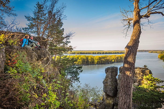 Zwei Wanderer genießen im Herbst den Ausblick vom Sentinel Rock im Mississippi Palisades State Park bei Savanna, Illinois, mit Blick auf den Mississippi River.