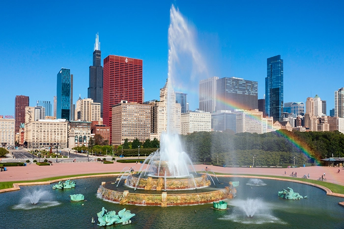 Die Buckingham Fountain im Grant Park in Chicago mit Blick auf die Skyline und einem Regenbogen über den Wasserfontänen.