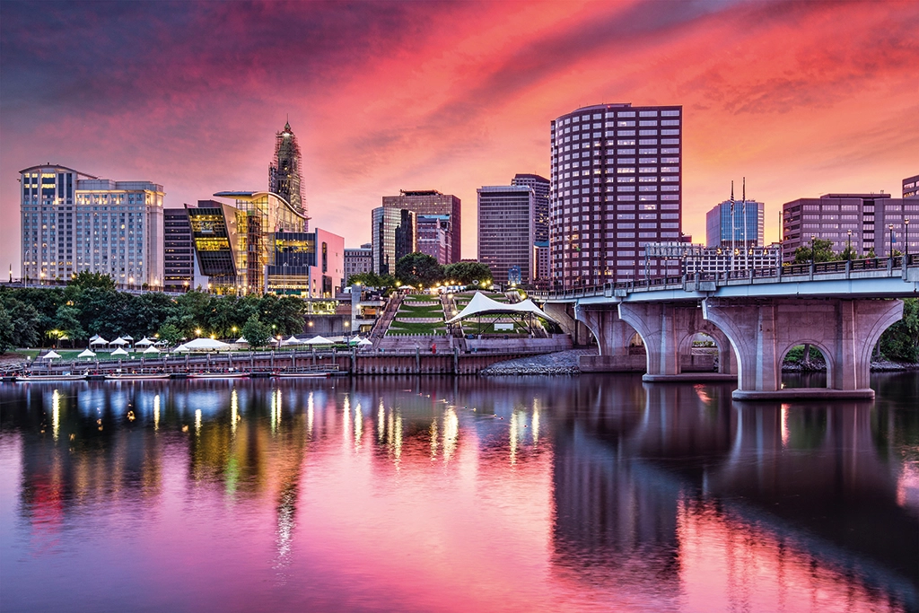 Blick auf die Skyline von Hartford, Connecticut, bei Sonnenuntergang mit reflektierenden Hochhäusern am Ufer des Connecticut River.