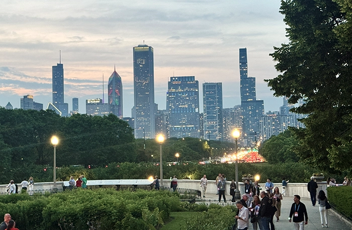 Abendstimmung über der Skyline von Chicago, gesehen vom Field Museum aus, mit Spaziergängern im Vordergrund und beleuchteten Hochhäusern im Hintergrund.