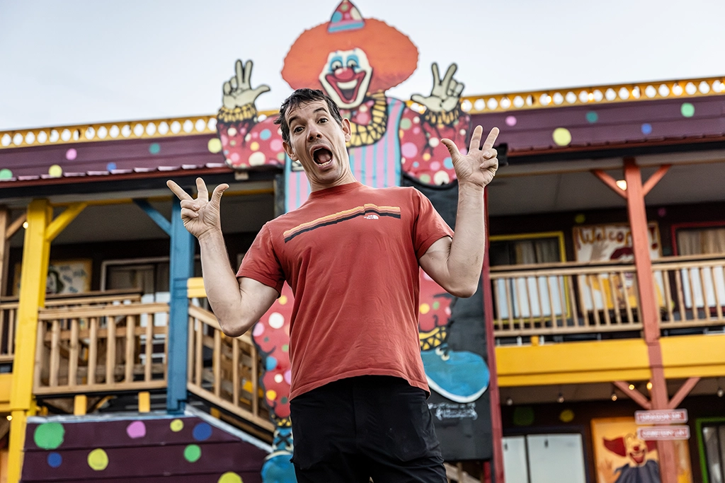 Alex Honnold posiert lachend vor dem bunten Clown Motel in Tonopah, Nevada, bekannt für seine exzentrische Fassade.